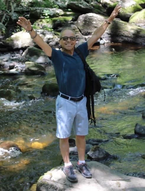 Harold standing on rocks with his arms raised by a stream